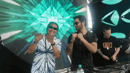 a man wearing a tie dye shirt is standing in front of a dj