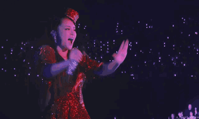 a woman in a red sequined dress is holding a microphone with her arms in the air