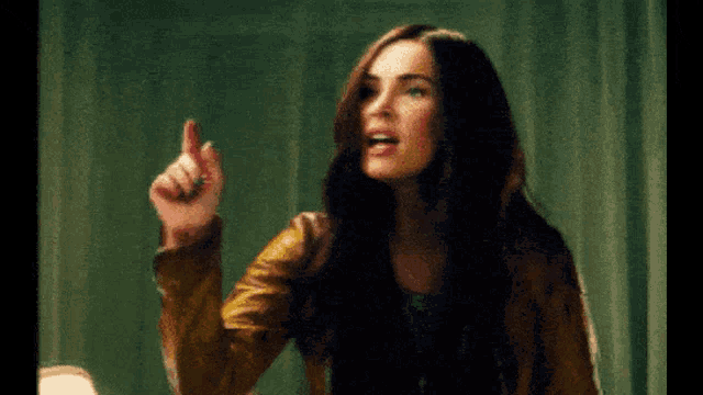 a woman in a brown leather jacket is pointing up with her finger
