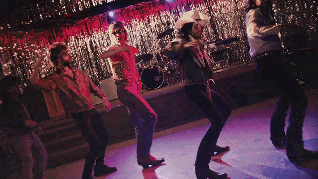 a group of people are dancing on a stage and one of them has the word cowboy on his back