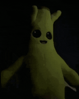 a green stuffed animal with big eyes is standing in the dark in a dark room .