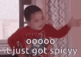 a young boy in a red shirt is standing in front of a window and says `` it just got spicyy '' .