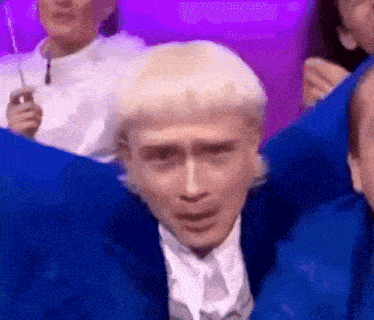 a man with blonde hair and a blue jacket is making a funny face .