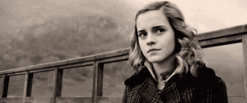 a black and white photo of a young woman standing on a bridge looking at the camera .