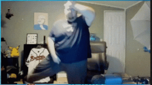 a man in a blue shirt is dancing in a room with a baseball jersey that says braves on it