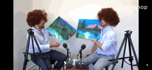 two men are sitting in front of microphones holding up paintings and the word ideashop is on the bottom right
