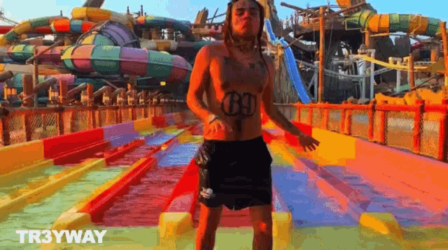 a man with a tattoo on his chest stands in front of a water slide at a water park with the words tr3yway above him
