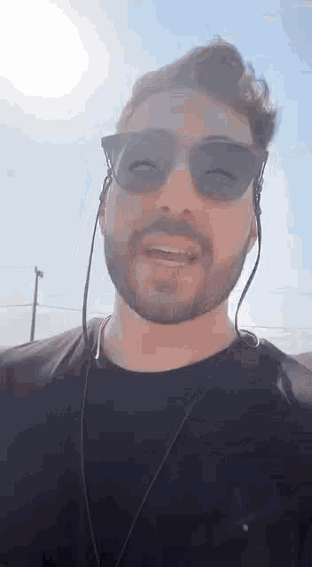 a man with a beard wearing sunglasses and headphones is talking to the camera .