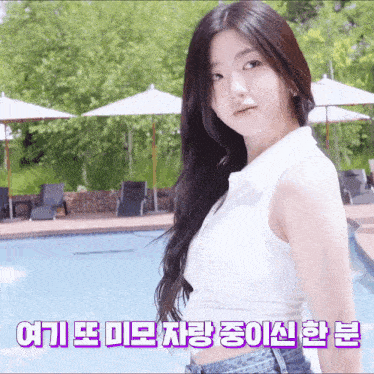 a woman in a white tank top is standing in front of a pool with umbrellas and chairs .