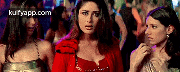 a woman in a red dress is standing next to two other women in a crowd .
