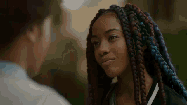 a woman with braids looks at a man with a smile on her face .