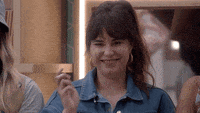 a woman in a denim jacket is smiling while holding a cigarette in her hand .