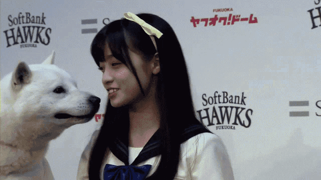 a girl and a white dog are standing in front of a softbank hawks sign