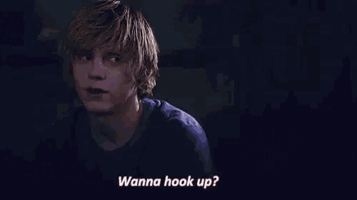 a young man in a blue shirt is talking to someone in the dark .