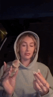 a woman in a hooded sweatshirt is holding a piece of food in her hands .
