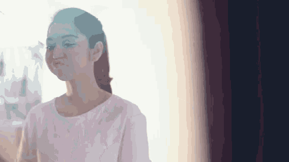 a woman in a white shirt is standing in front of a window making a funny face .