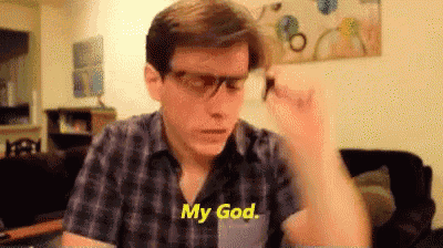 a man wearing glasses and a plaid shirt is sitting in a living room and saying `` my god '' .