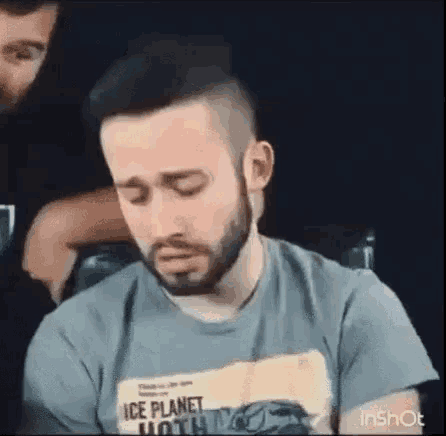 a man with a beard is sitting in a chair with his eyes closed and a t-shirt on .