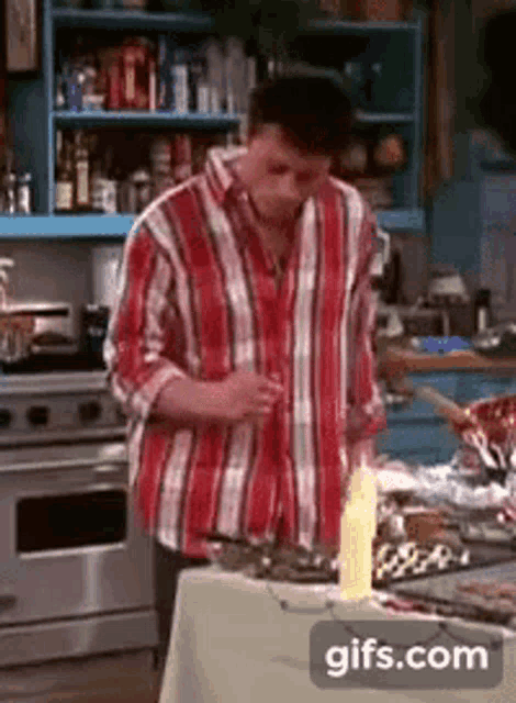 a man in a red and white striped shirt is standing in a kitchen with a candle on a table .