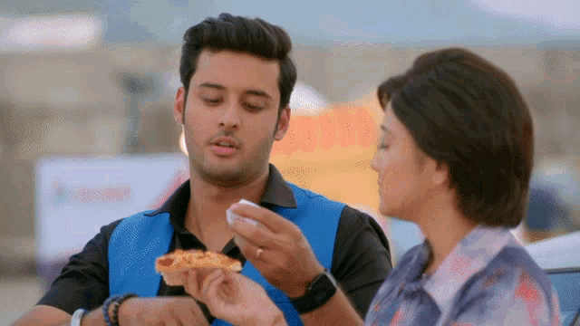 a man in a blue vest is feeding a woman a pizza