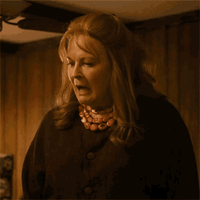a woman is wearing a necklace and a brown jacket