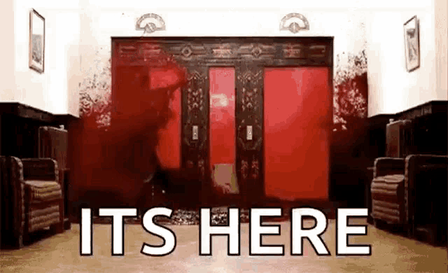a room with a red door and the words `` it 's here '' written in white letters .