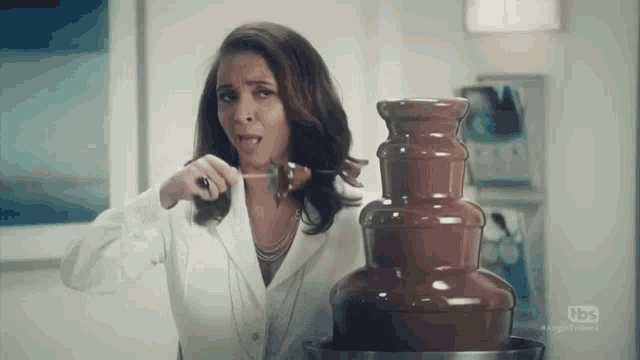 a woman is standing in front of a chocolate fountain and eating a piece of chocolate