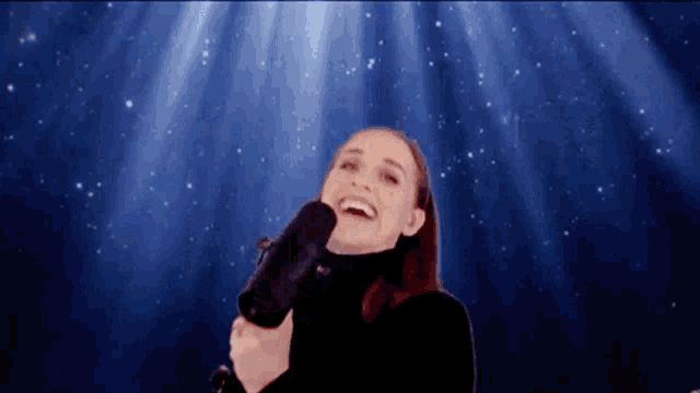 a woman in a black turtleneck is holding a microphone and laughing