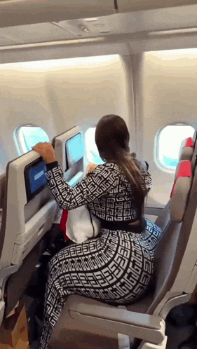 a woman sits on an airplane looking at a monitor