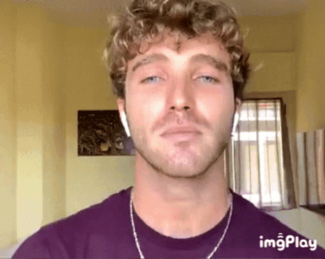 a man with curly hair and a beard is wearing headphones and a purple t-shirt .