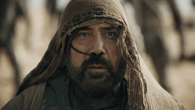 a man with a beard and a scarf around his head looks at the camera