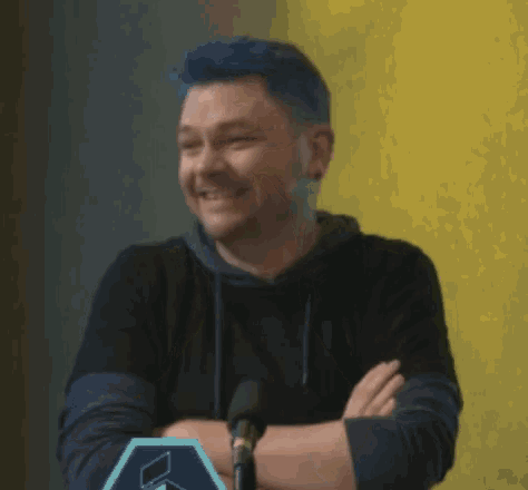 a man with blue hair is covering his mouth with his hands in front of a microphone