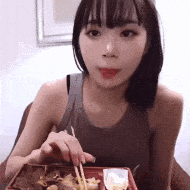 a woman is eating food with chopsticks from a box .