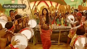 a woman in a red dress is dancing in front of a crowd of people playing drums .