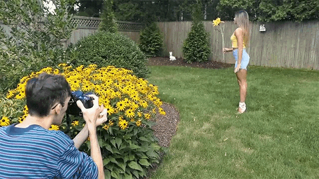 a man is taking a picture of a woman in a garden with a camera .