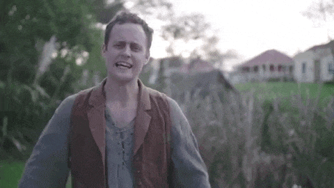 a man in a brown vest is standing in a field with his arms outstretched .