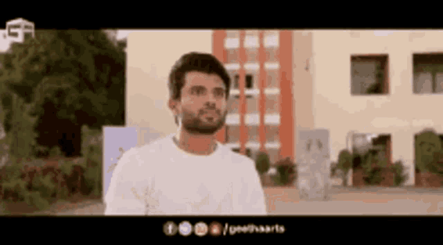 a man with a beard is standing in front of a building in a white shirt .