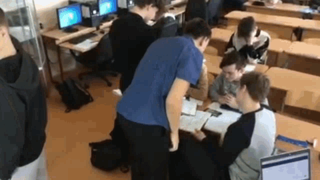 a group of young men are sitting at desks in a classroom with computers .
