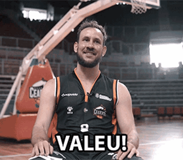 a man in a basketball uniform is sitting in front of a basketball hoop with valeu written on the ground