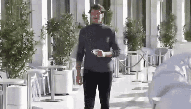 a man is walking down a sidewalk holding a cup of coffee in his hand .