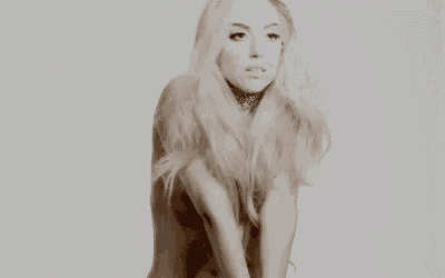 a naked woman with long blonde hair and a choker is smiling and dancing in a black and white photo .