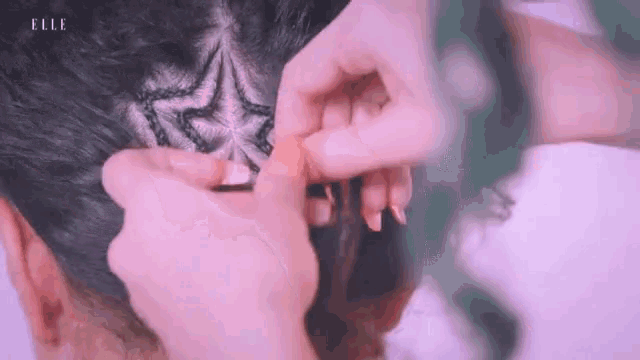 a person is braiding a woman 's hair with a pink background