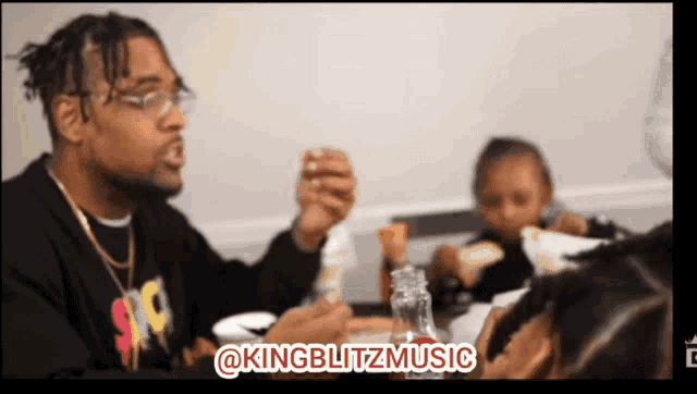 a man sitting at a table with a bottle of kingblitz music on the bottom right