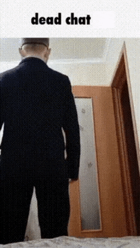 a man in a suit is standing in front of a door with the words `` dead chat '' written on it .