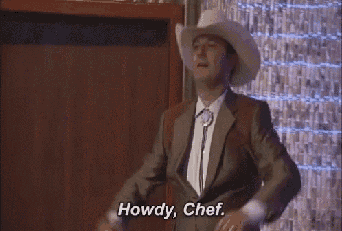a man in a cowboy hat and suit is standing in front of a wall and saying howdy , chef .