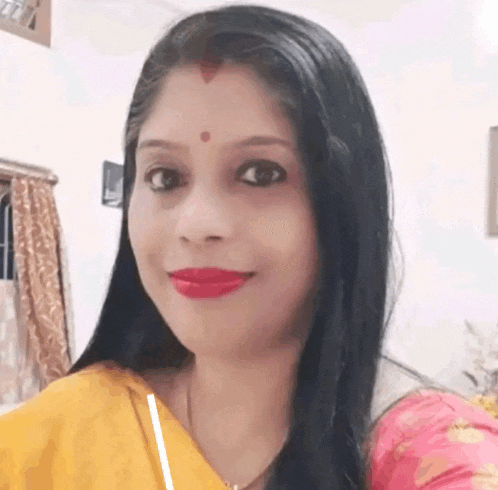 a woman with long black hair is smiling for the camera while wearing a yellow and pink dress .