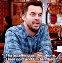 a man in a plaid shirt is talking on a cell phone while sitting in a bar .