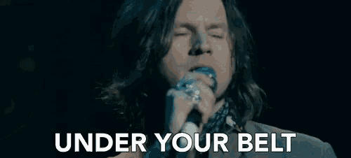 a man singing into a microphone with the words under your belt written below him .