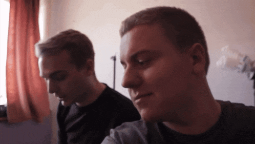 two men are sitting in front of a window and one of them is looking down