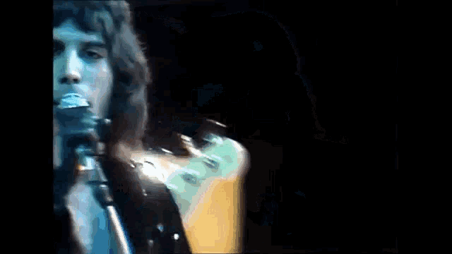 a man is singing into a microphone while another man plays a bass guitar .